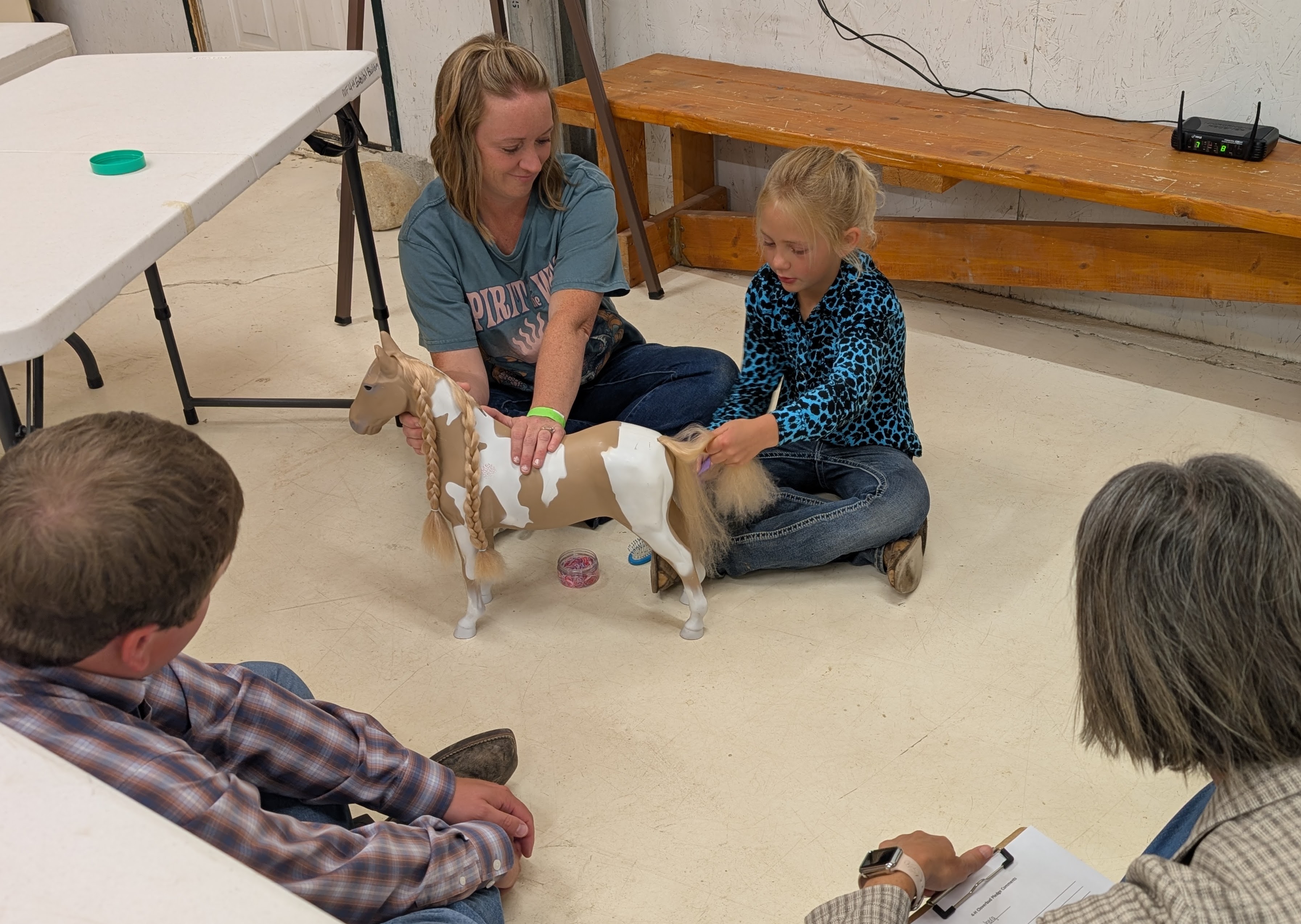 A Cloverbud shows how to braid hair on a toy horse the judges sitting with her on the floor to lower her fear.